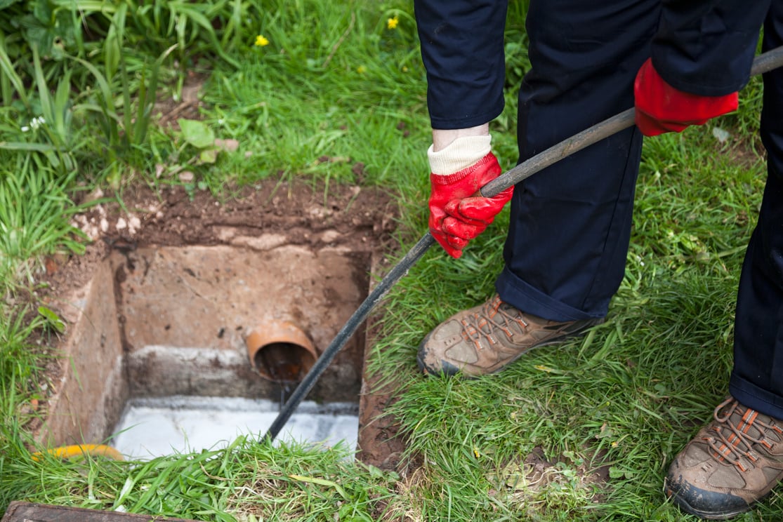 Man with ground open unblocking a drain with a tool